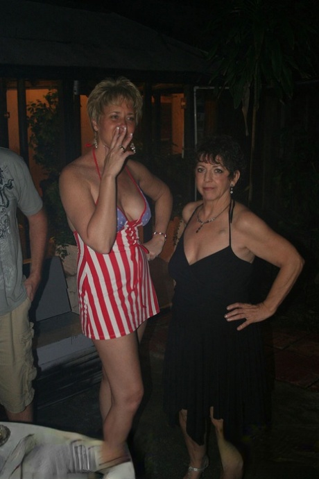 Playful amateur mature swinger wives teasing and French kissing at a party