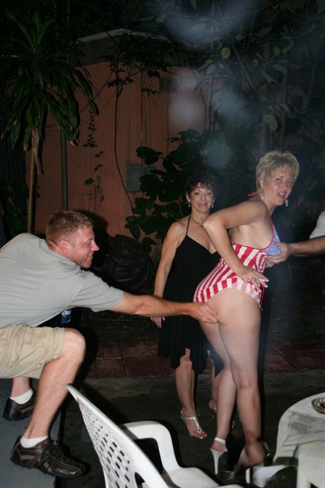 Playful amateur mature swinger wives teasing and French kissing at a party